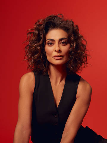 Juliana Paes *** Local Caption *** mulher com cabelo cacheado e volumoso, vestindo um colete preto sem mangas e calças pretas.